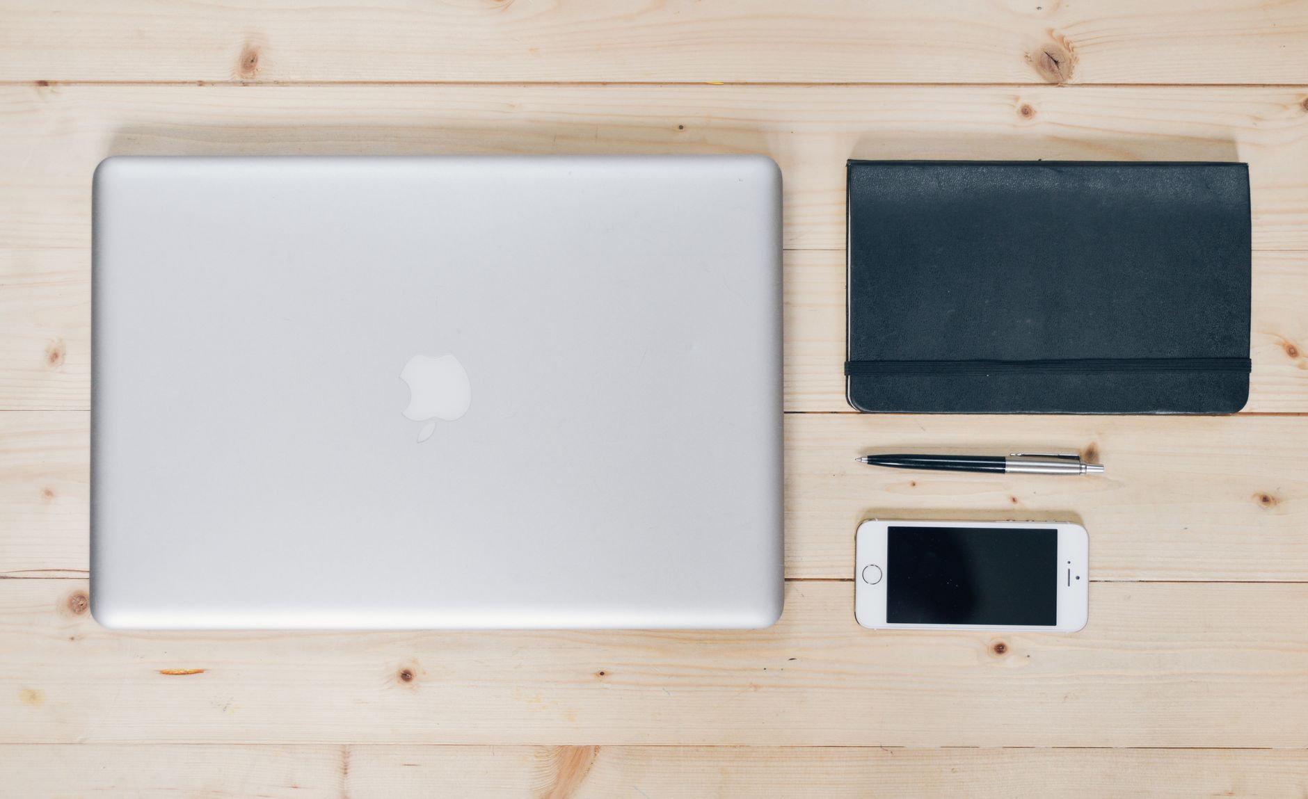 A clean, organized desk featuring a laptop, smartphone, notebook, and pen, ideal for productivity.