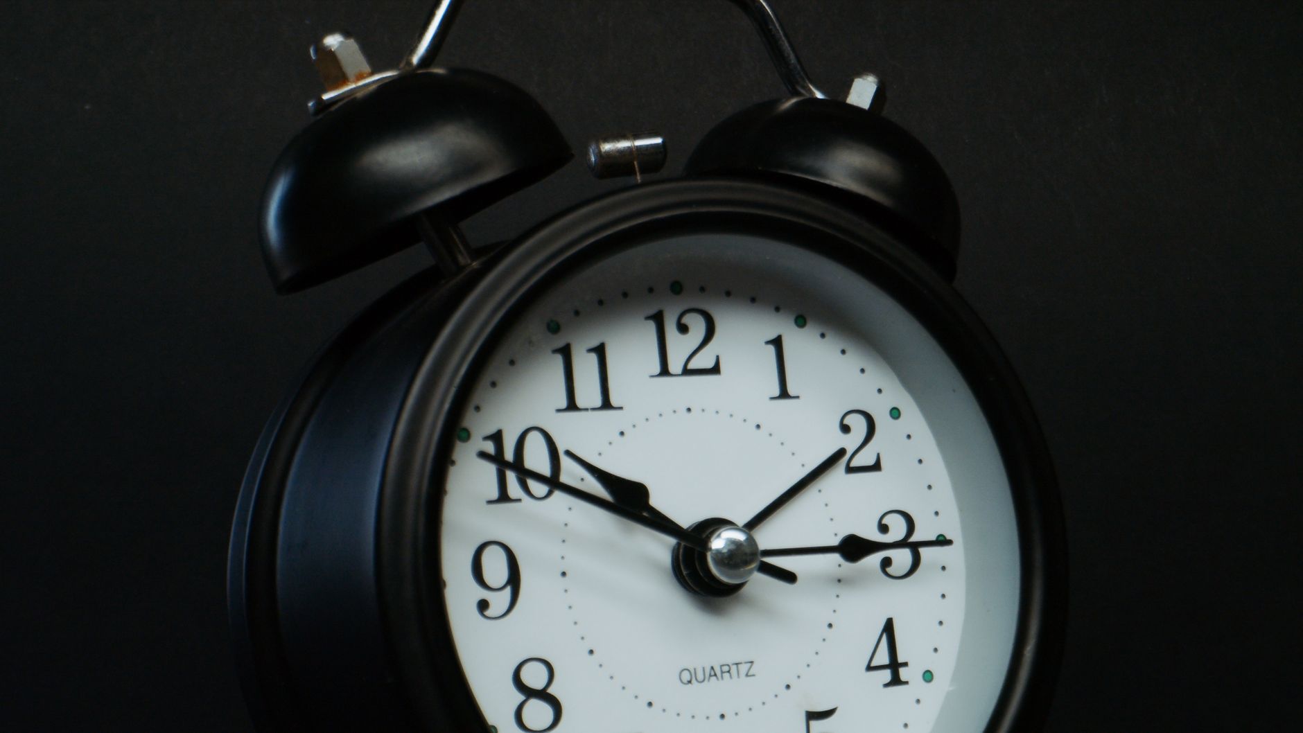 Close-up of a vintage black alarm clock against a dark background, showing the time at 10:10.