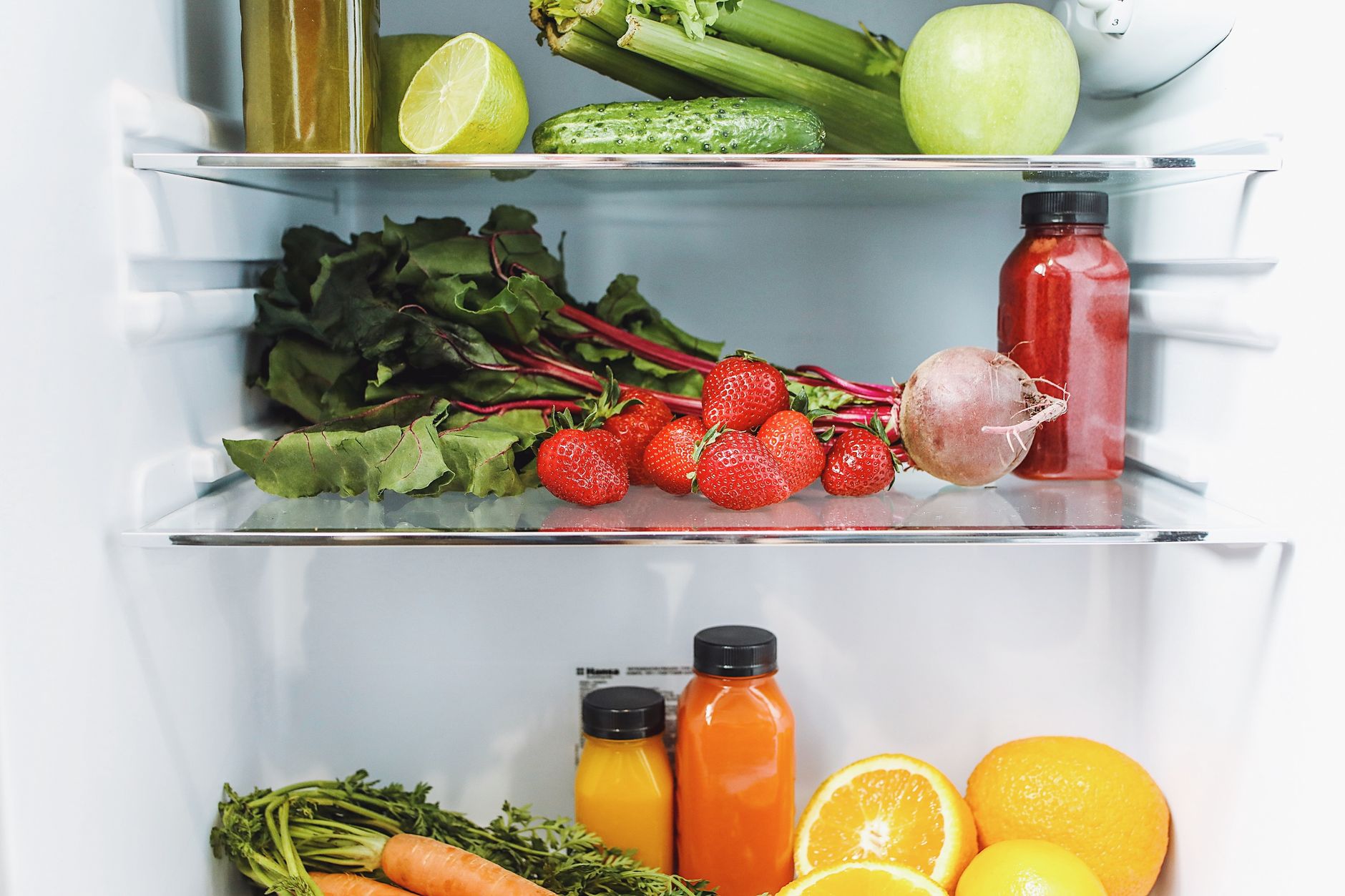 Open refrigerator with vegetables, fruit, and drinks arranged on shelves.