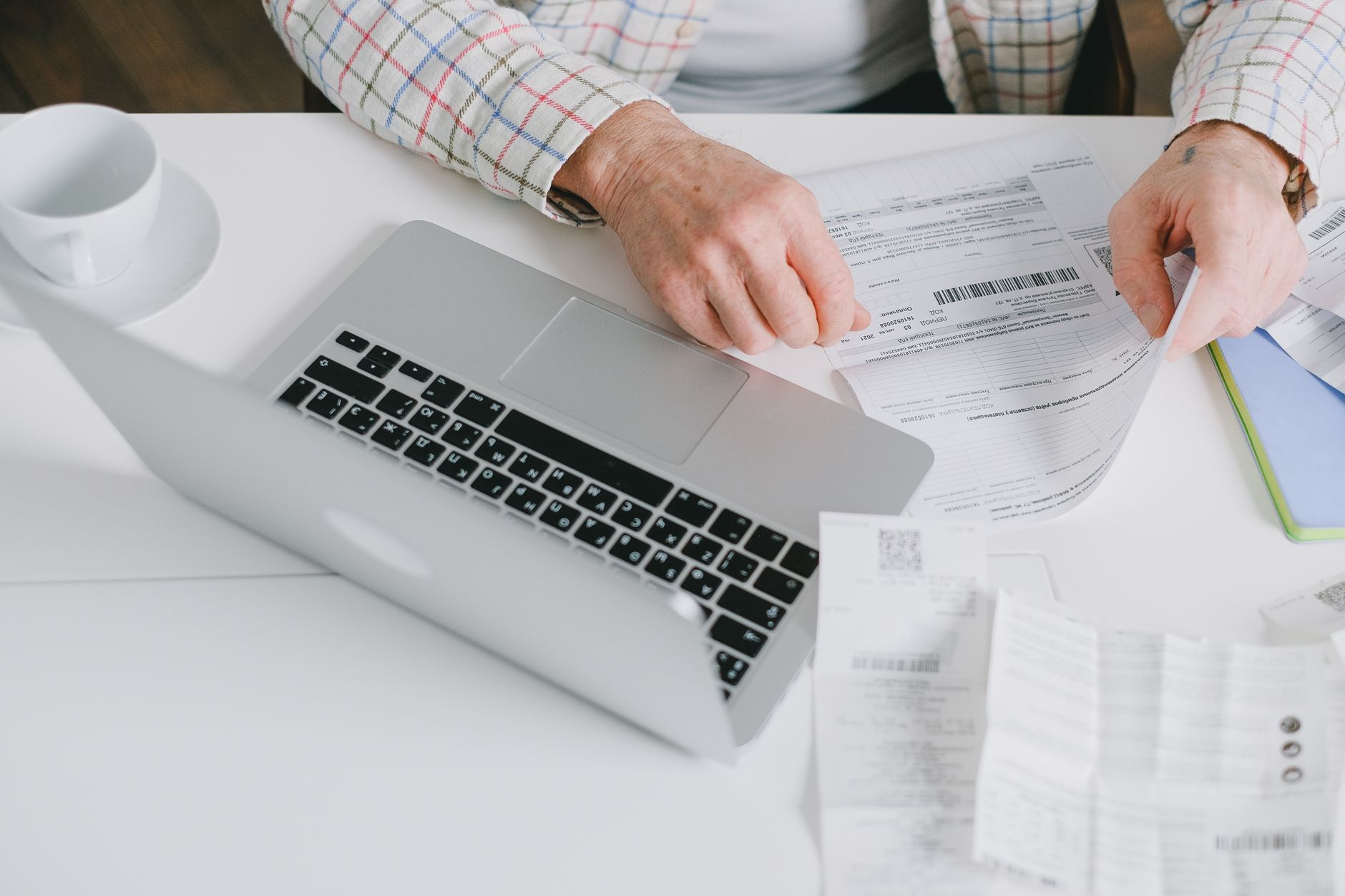 Person sorts paper bills and receipts beside a laptop.